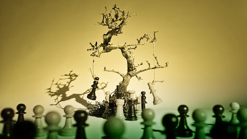 Tree with hanging chess pieces surrounded by pawns.