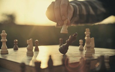 A person leans forward with intense focus, his hand hovering over the chessboard as they make a bold move, seizing control of the game with aggressive tactics.