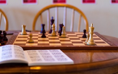 Chess pieces on chessboard with open tactics book in front.