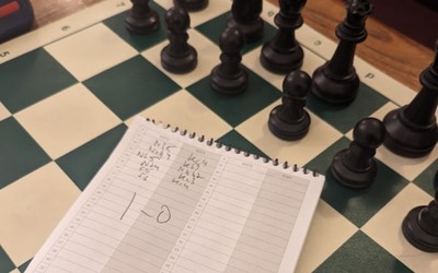 Scoresheet indicating a hard-fought win as white after 50+ moves, on top of a chess board with black pieces at Marshall Chess Club, NYC