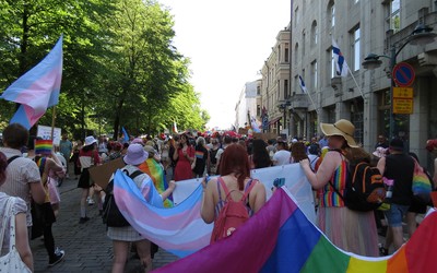 People marching during pride in a city carrying trans and rainbow flags