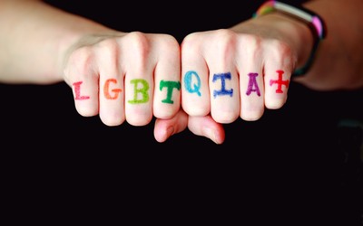 the letters LGBTQIA+ written in rainbow colors on the back of the fingers while the person's fists are clutched
