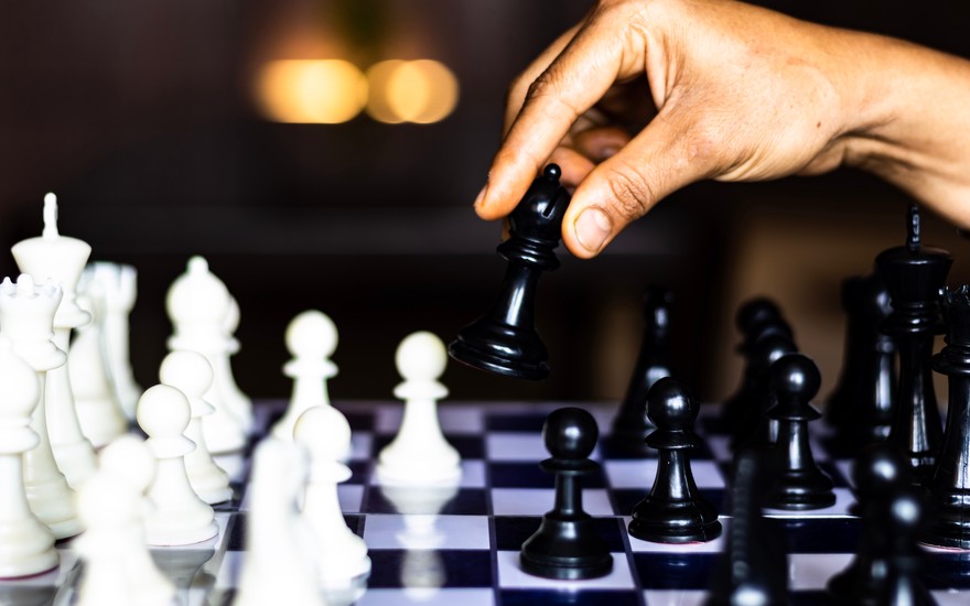 Person moving black bishop on chess board.